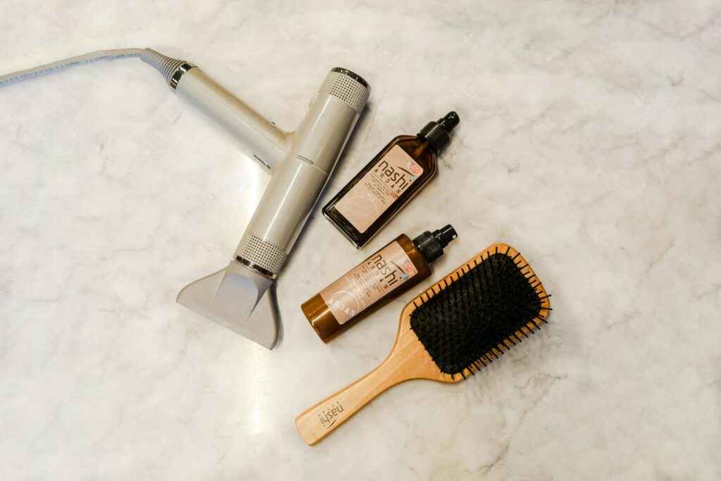 Flat lay of hairdryer, hairbrush, and styling products on a marble table.